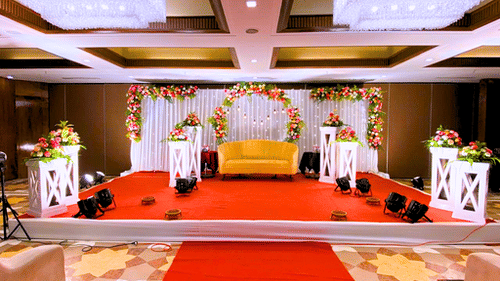 A grand wedding stage setup at Pride Plaza Ahmedabad, featuring a floral backdrop, a sofa, and a red carpet leading to the stage.